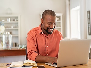 smiling black man working on his computer to refinance his mortgage